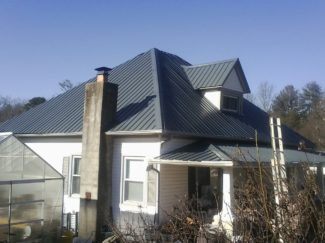 Dark blue standing seam metal roof on a white farmhouse with dormer — Slate & Tile Roof Repair by Roofing Brothers in Homeland