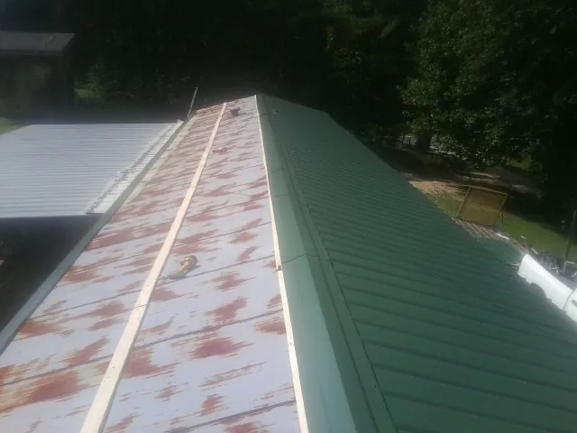 Old rusted panels beside newly installed green metal roofing — Wind Damage Roof Repair by Roofing Brothers in Homeland